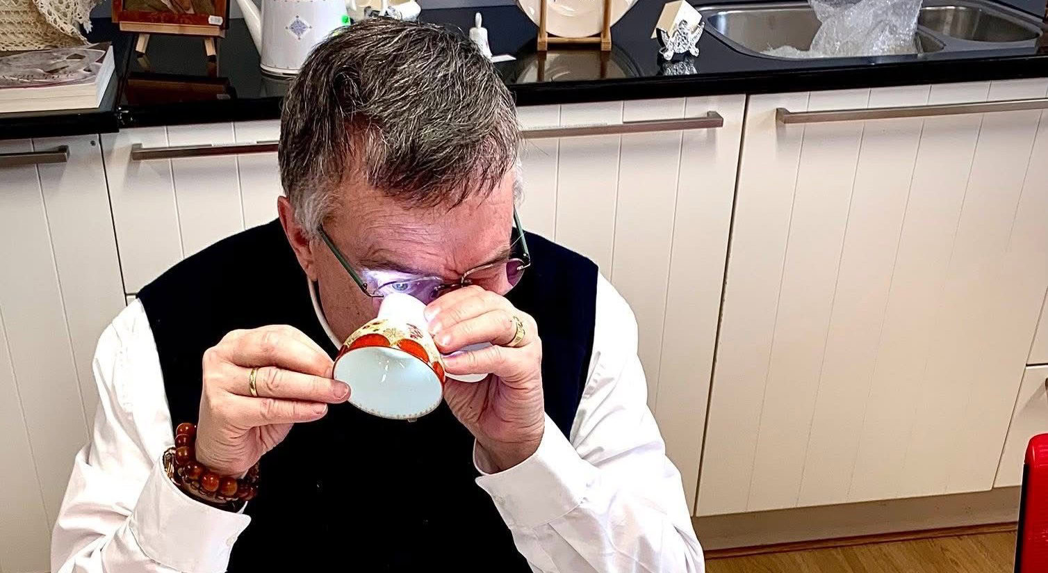 Man drinkt uit een kopje in een keuken met witte kasten en zwarte werkblad.