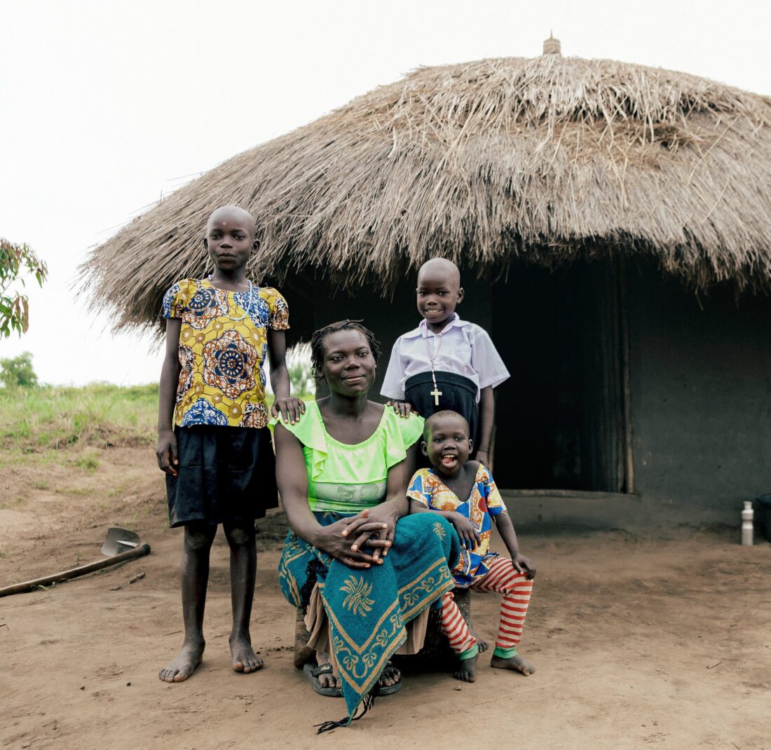Vrouw met drie kinderen voor traditionele hut in een landelijke omgeving in Afrika.