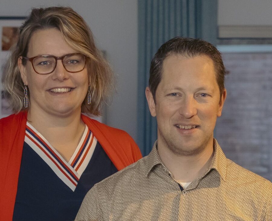 Twee mensen staan samen in een kantooromgeving en lachen naar de camera.